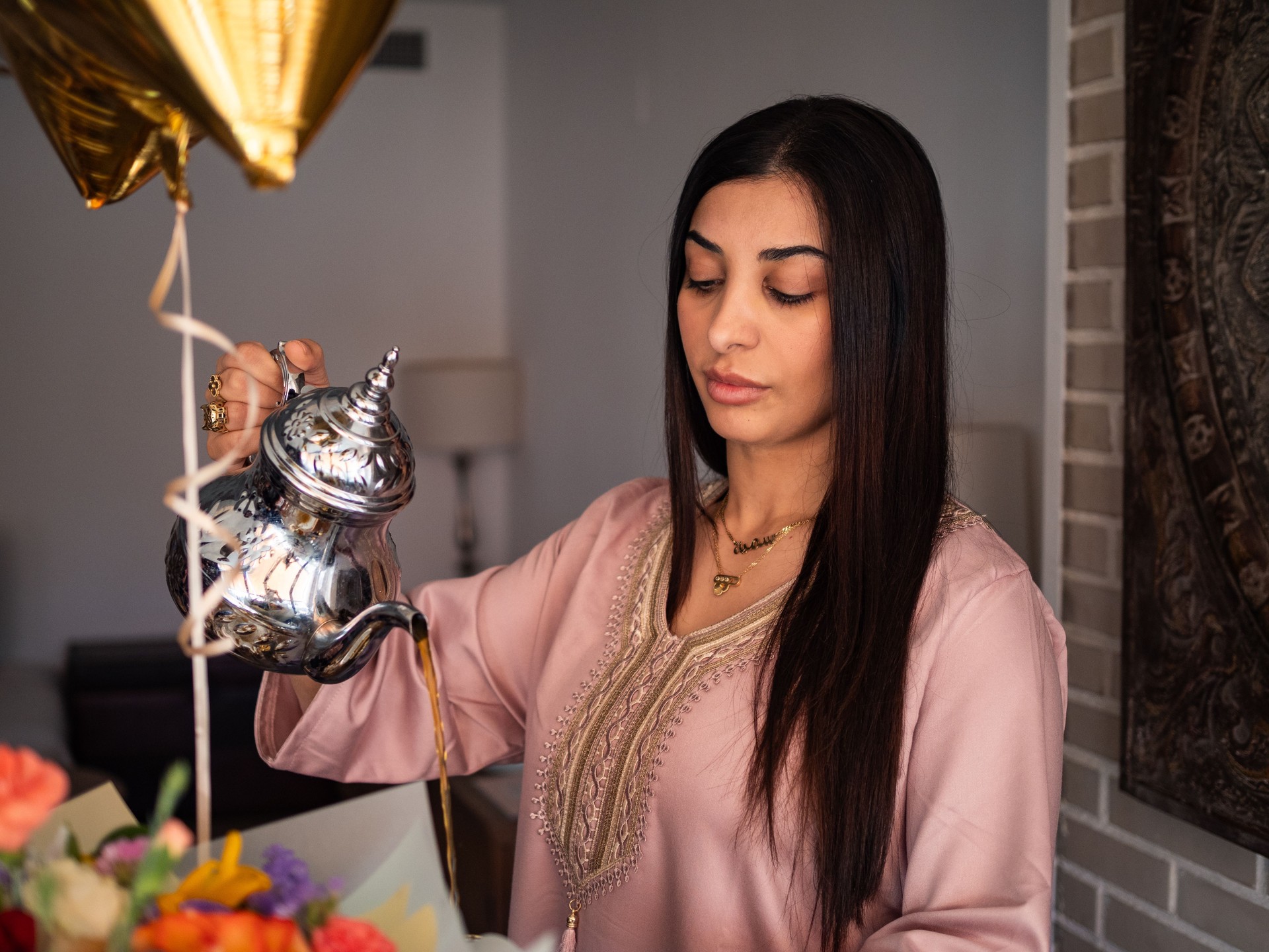 Arabic woman pours tea from a silver pot during a celebration with flowers and a balloon